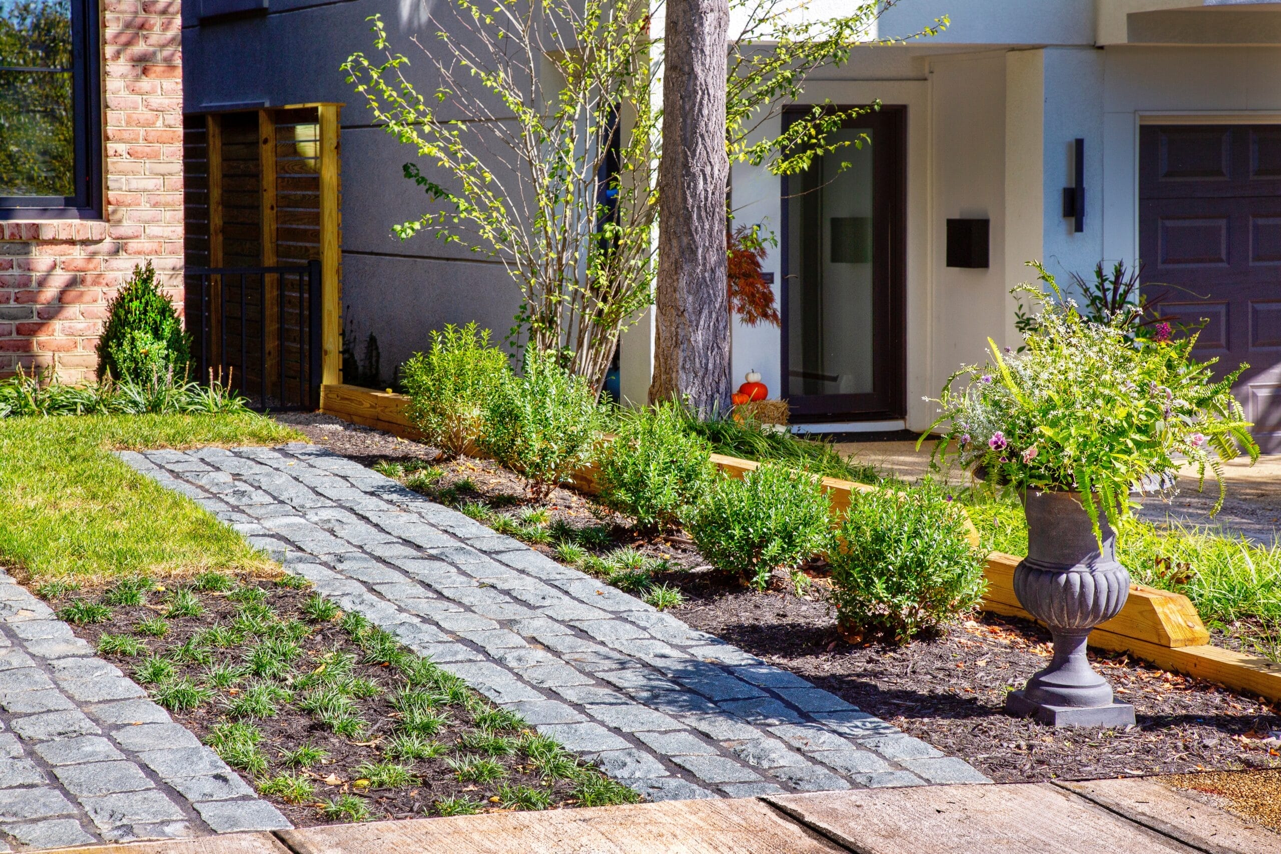 Paver walkway with grass strips leading to modern home entrance with landscaped beds and decorative urn - Ridge