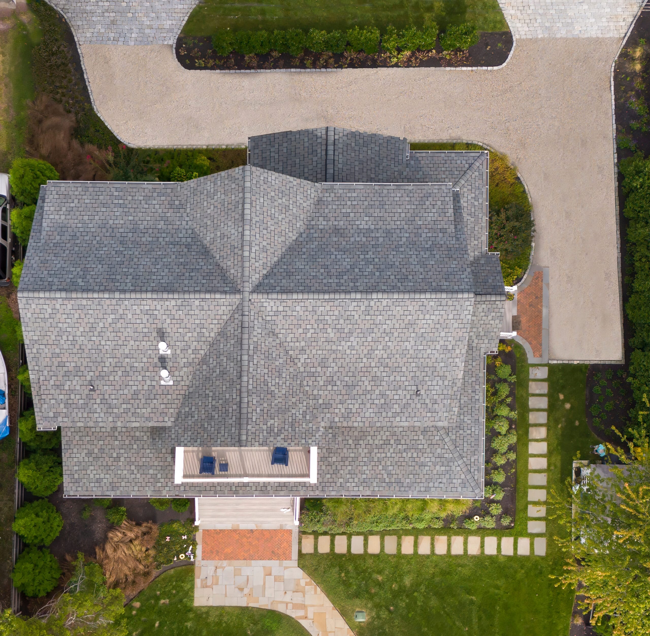 Aerial view of gray shingled roof with rooftop deck, landscaped yard, paver walkway, and driveway by Ridge