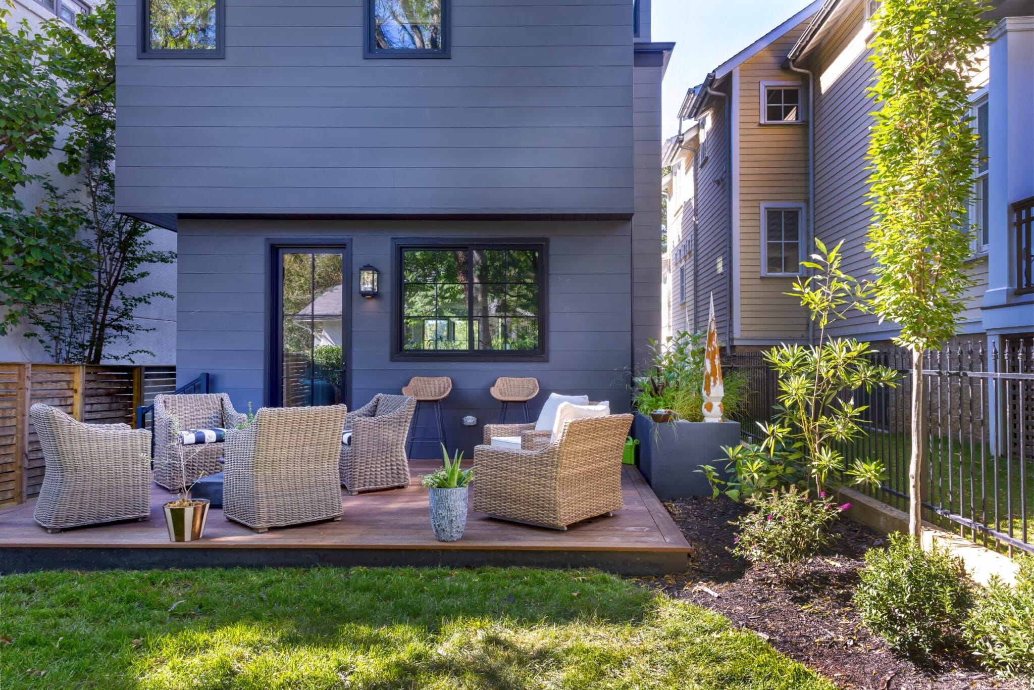Wooden deck with wicker outdoor furniture and landscaped planters outside blue modern home - Ridge