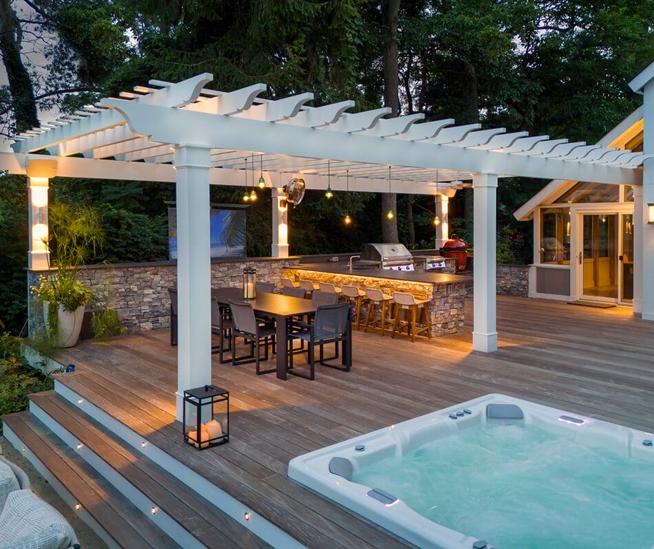 White pergola with string lights, stone outdoor kitchen bar, composite deck, and hot tub - Ridge