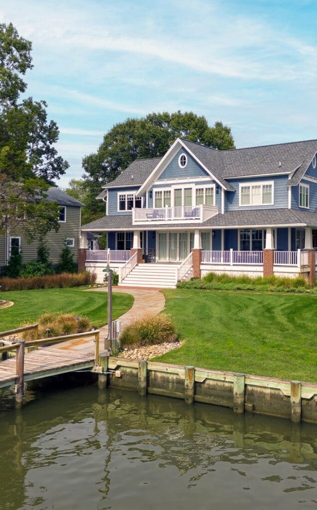 Blue coastal home with white trim, wraparound porch, private dock, and waterfront lawn by Ridge